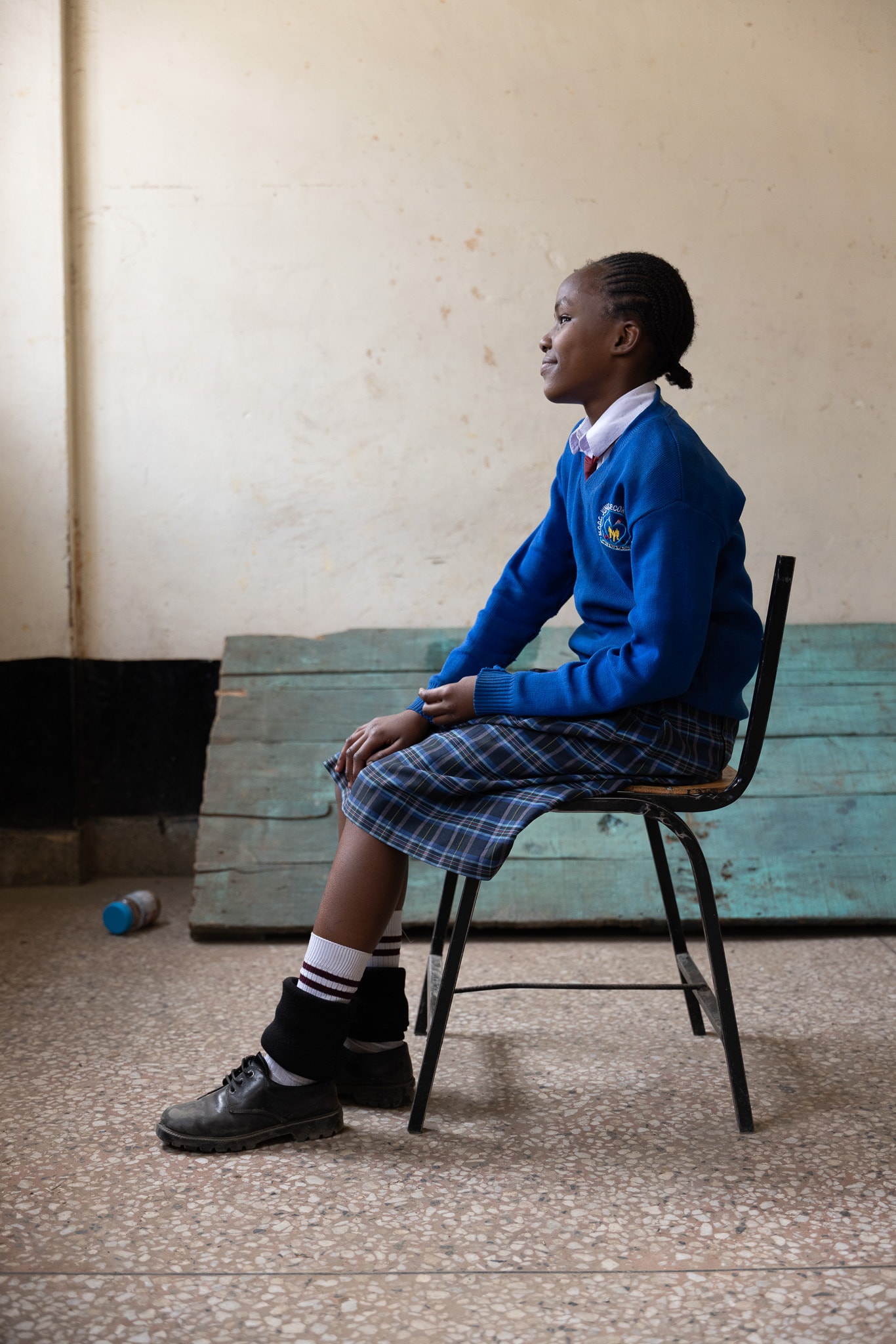 Student in blue school uniform seated on a chair, profile view